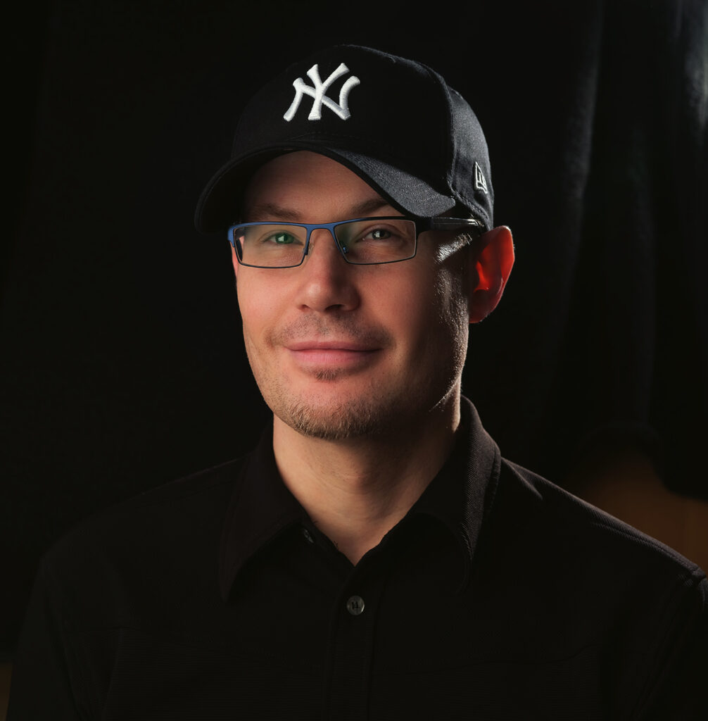 Man wearing a cap and glasses against a dark background.