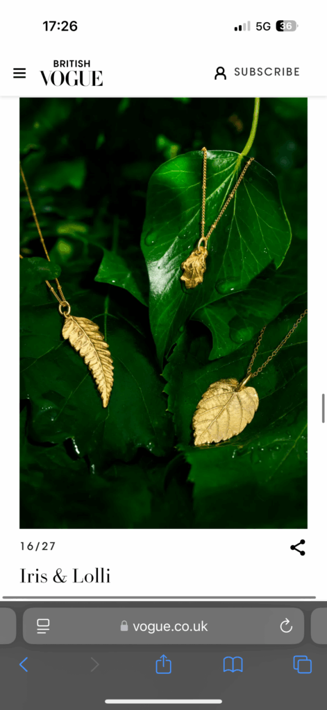 Gold handmade leaf-shaped jewellery resting on green leaves with raindrops, featured in Vogue.