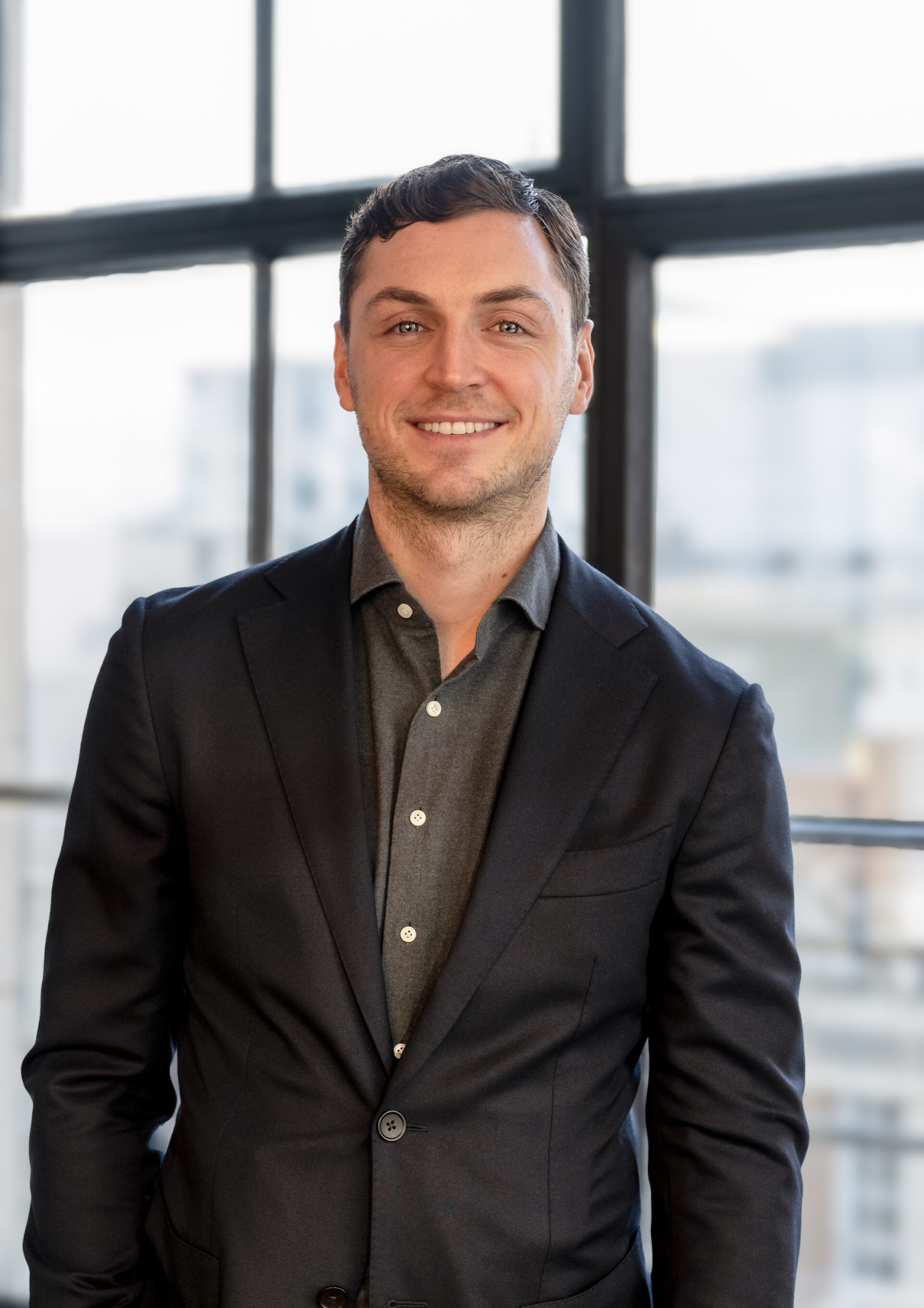 Professional office headshot of a man in a suit standing in front of a window with natural light.