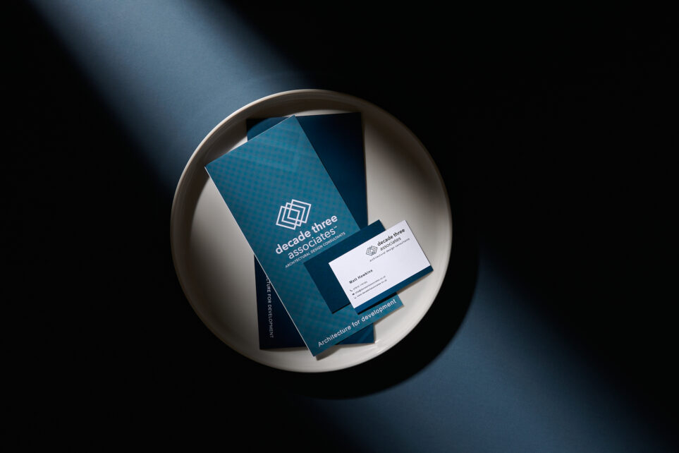 Brochure and card placed on a tray with dramatic shadows cast over them.