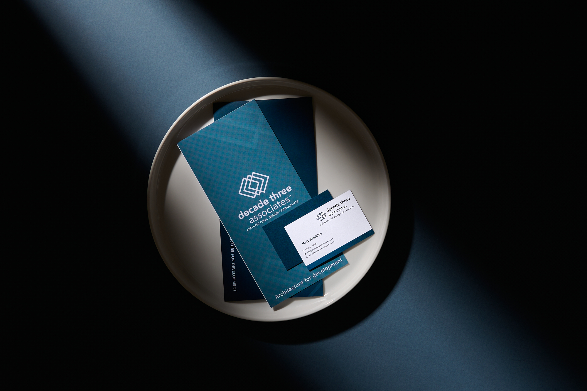 Brochure and card placed on a tray with dramatic shadows cast over them.