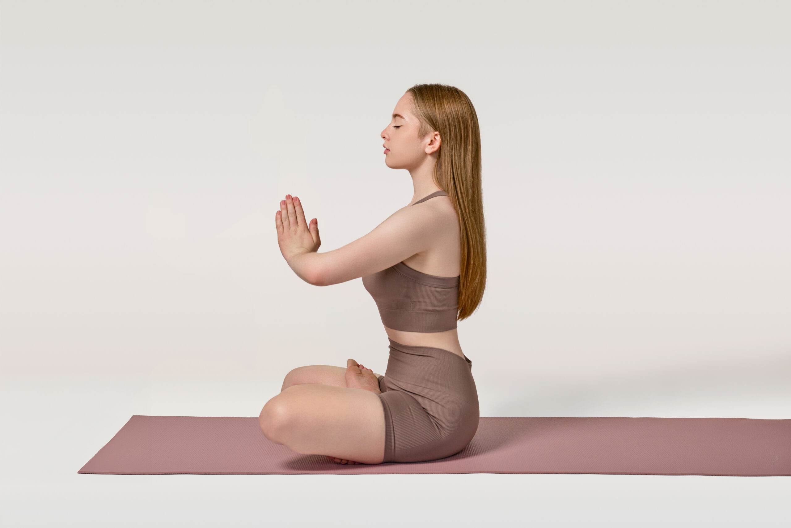 Woman sitting in a yoga position on a pink yoga mat in a bright, airy room, radiating calmness and mindfulness.